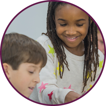 A multi-ethnic group of elementary school students are indoors in a school classroom  They are wearing casual clothing  They are working with tablets to learn computer programming  A girl of African descent is helping her Caucasian friend 